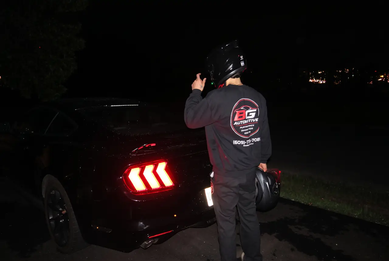 BG Automotive technician with black Mustang at night